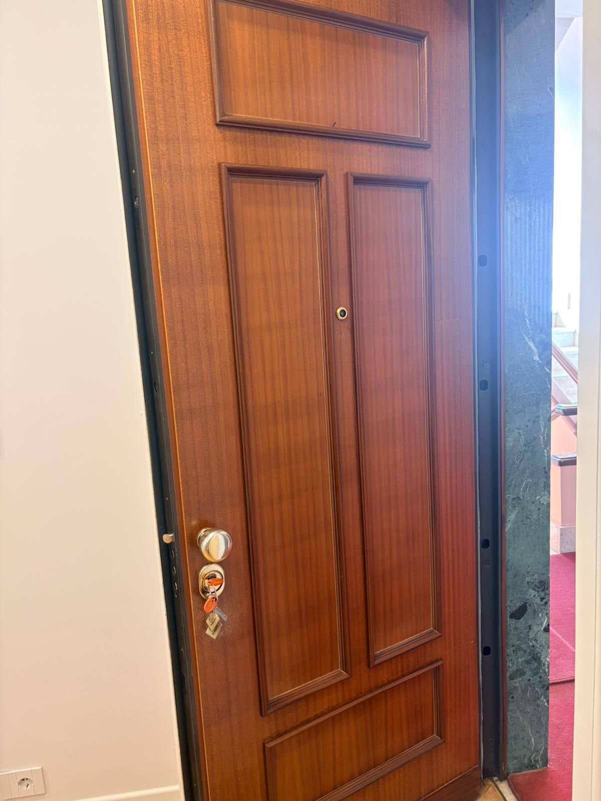 Porta d'ingresso in legno con pannelli, spioncino e chiavi inserite nella serratura a cilindro europeo